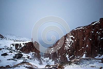 Frozen waterfall on the background of hills on the Kola Peninsula and a man standing on the edge of the cliff and looking into the Stock Photo