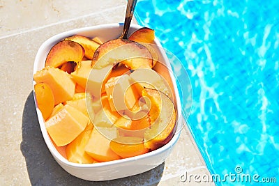 Fruit in a bowl by the pool. Fruit salad, healthy breakfast. Colorful fruit peach and melon, summer concept Stock Photo