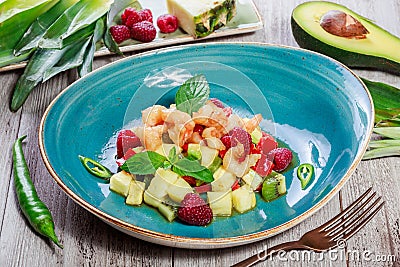 Fruit salad with shrimp, avocado, bulgarian pepper, kiwi, pineapple, raspberries in plate on wooden background close up. Stock Photo