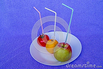 Fresh green apple, yellow orange and red tomato lying on a white plate with straws of corresponding colors on purple background Stock Photo