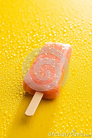 Fruity ice lolly. Sweet popsicle on yellow table with water drops Stock Photo