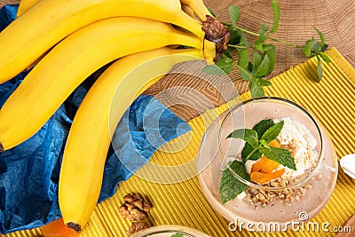 Fruity smoothie in dessert glass with a branch of bananas on a yellow and blue background. Cocktails with dried apricots Stock Photo