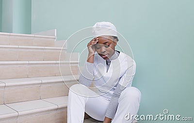A frustrated African-American nurse is sitting in a hospital corridor. The medical worker looks unhappy. A picture of a Stock Photo