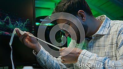Frustrated Arabian Indian man programmer holding paper code bills problem checking information data monitor computer Stock Photo