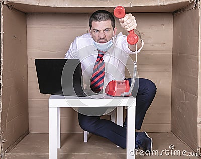 Frustrated businessman sits in his cramped cardboard office and is having an aggressive conversation on the phone Stock Photo
