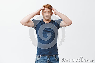 Frustrated gloomy redhead male in blue t-shirt, holding head and staring with disappointment at camera, losing bet Stock Photo