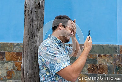 Frustrated hipster man feeling upset desperate, receiving social media news on the smart phone. Guy crying after read a message of Stock Photo