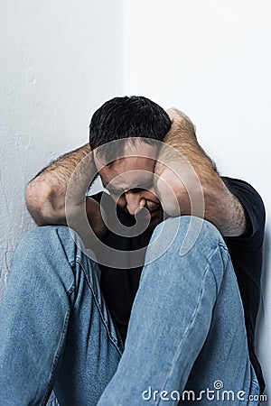 Frustrated man suffering while sitting in corner and holding hand on head Stock Photo