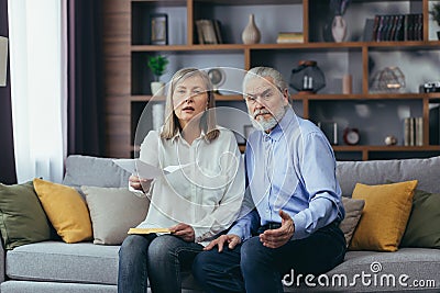 Frustrated married couple, retired man and woman, sitting on sofa at home, frustrated with document and letter, looking at camera Stock Photo