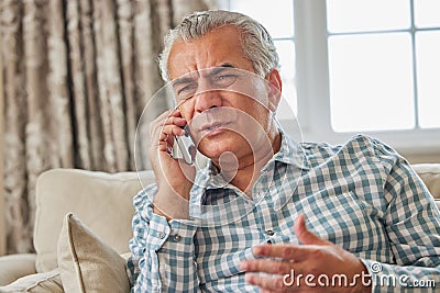 Frustrated Mature Man Receiving Unwanted Telephone Call At Home Stock Photo