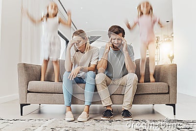 Frustrated parents, sofa and headache with children jumping in living room chaos, ADHD or crazy home. Mother and father Stock Photo