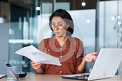 Frustrated and sad business woman holding financial report in hands, Hispanic woman sad working in office using laptop Stock Photo