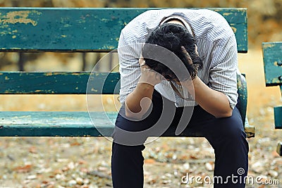 Frustrated stressed Asian business man with hand cover face sitting on the bench of public park and suffering from depression and Stock Photo