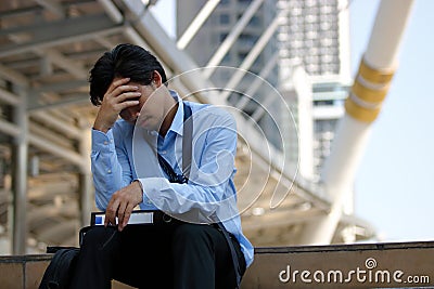 Frustrated stressed Asian businessman with hand on forehead sitting on staircase in the city. Depressed unemployment business conc Stock Photo