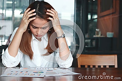 Frustrated stressed young Asian business woman analyzing paper work or charts in workplace. Thinking and thoughtful concept. Stock Photo