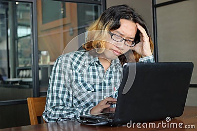 Frustrated stressed young Asian hipster worker touching on head and looking laptop in office. Stock Photo