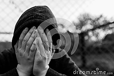 Frustrated teenage boy covering hes face in front of correctional institutes wired fence, conceptual image of juvenile delinquency Stock Photo