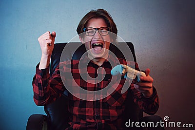 Frustrated teeneager playing video games seated on his armchair. Angry and furious guy gesturing with hand while holding the Stock Photo