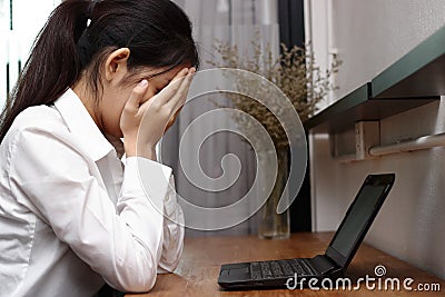 Frustrated tired young Asian woman with hands on face in workplace of office Stock Photo