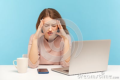Frustrated tired young woman employee sitting at workplace with laptop and holding painful head, suffering migraine Stock Photo