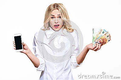 Frustrated woman shrugging shoulders, showing mobile phone blank screen and holding loads of Euro banknotes on white background. Stock Photo