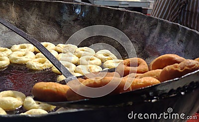 Frying Donuts in hot oil by a iron carrier in a village fair Stock Photo