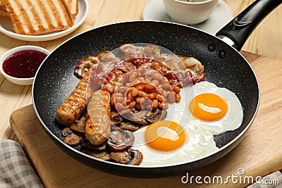 Frying pan with cooked traditional English breakfast on wooden table, closeup Stock Photo