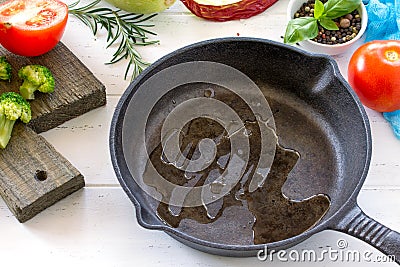 Frying pan made of cast iron, various fresh vegetables and spices on a white wooden kitchen table. Culinary background Stock Photo