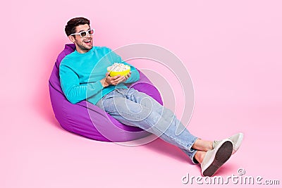 Full body photo of attractive young guy sitting beanbag 3d glasses eat popcorn wear trendy blue clothes on pink Stock Photo