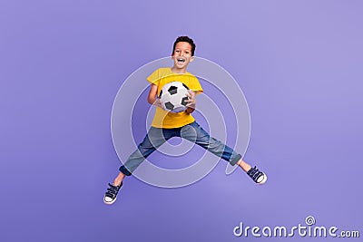 Full body photo of charming young boy hold soccer ball jumping playful wear yellow outfit isolated on purple color Stock Photo