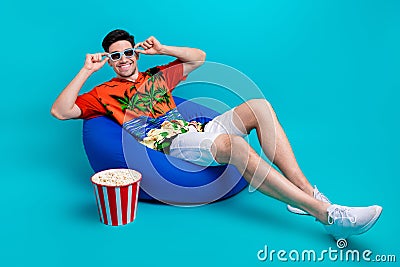 Full body photo funny young guy wear 3d goggles watching funny comedy sitting beanbag eat popcorn chips isolated on blue Stock Photo