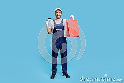 Full body portrait of excited happy courier in uniform holding shopping bags and credit card, studio shot Stock Photo