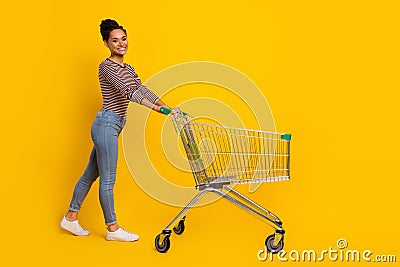 Full body profile photo of attractive positive girl walk push trolley isolated on yellow color background Stock Photo