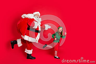 Full body profile side photo of cheerful two fairy runners santa claus elf in hat headwear carrying heavy bag with Stock Photo