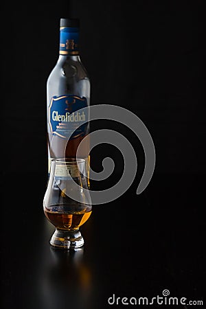 A full glencairn glass and a bottle of scotch whiskey Editorial Stock Photo