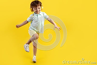 Full lengh photo of funny kid listening music in headphone and dance over yellow background. Stock Photo