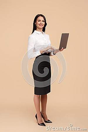 Full lengh photo of happy young modern business woman over beige background, working on laptop computer. Stock Photo