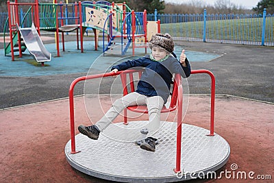 Full lengh portrait active school kid playing in park, Happy boy sitting on merry go round in playground, Child having fun outdoor Stock Photo