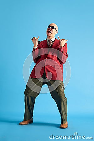 Full lenght image. Balded man with mustache dressed vintage dansing with call-sign and shouting over blue background. Stock Photo