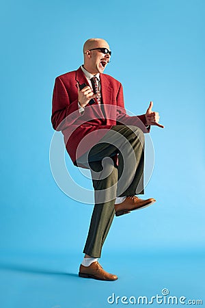 Full lenght image. Balded man with mustache dressed vintage dansing with call-sign and shouting over blue background. Stock Photo