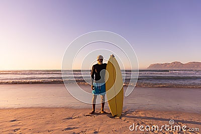 Full length of african american senior man with surfboard standing against seascape and clear sky Stock Photo