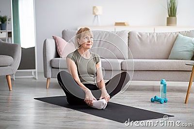 Full length of athletic mature woman stretching her legs, sitting in butterfly yoga pose on mat indoors, free space Stock Photo