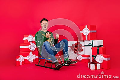 Full length body size photo happy guy in ugly sweater smiling sitting on sledges isolated bright red color background Stock Photo