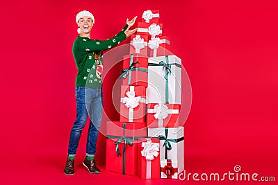 Full length body size photo overjoyed guy wearing festive cap showing present on xmas isolated vivid red color Stock Photo