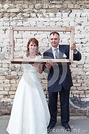 Full length of bride and groom looking through portrait frame Stock Photo