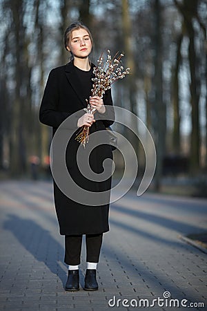 Full length emotional portrait of young happy beautiful woman with a bouquet of pussy-willows wearing black coat strolling at even Stock Photo
