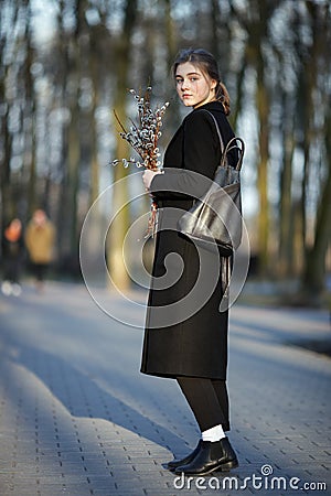 Full length emotional portrait of young happy beautiful woman with a bouquet of pussy-willows wearing black coat strolling at even Stock Photo