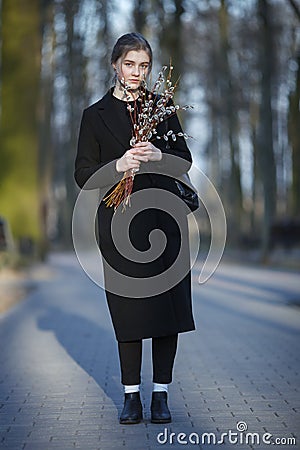 Full length emotional portrait of young happy beautiful woman with a bouquet of pussy-willows wearing black coat strolling at even Stock Photo