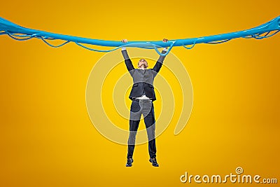 Full length front view of businessman hanging gripping at blue sticky slime thread on amber background. Stock Photo