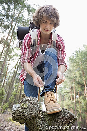 Full length of male backpacker tying shoelace in forest Stock Photo